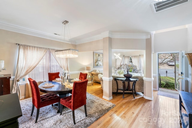 dining space with light hardwood / wood-style floors, ornamental molding, and an inviting chandelier