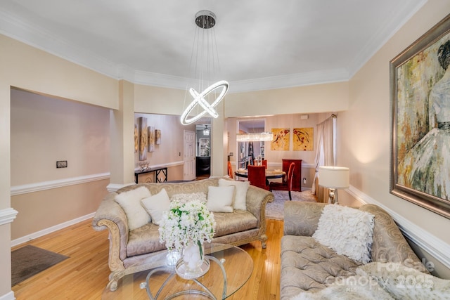 living area with a chandelier, ornamental molding, light wood-style flooring, and baseboards