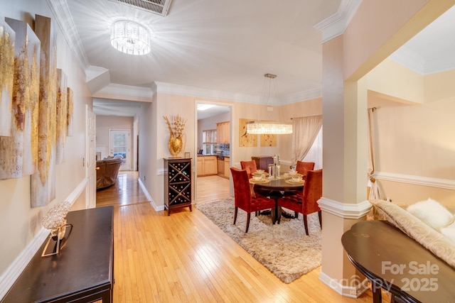 dining room with baseboards, light wood finished floors, visible vents, and crown molding