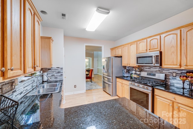 kitchen with light brown cabinets, stainless steel appliances, a sink, visible vents, and dark stone countertops