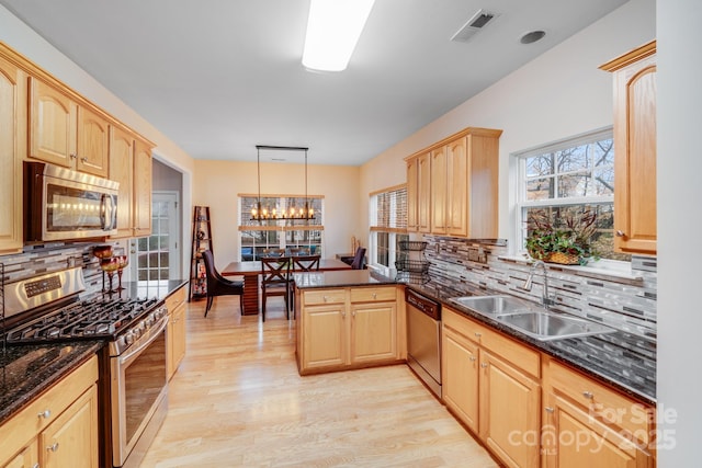 kitchen with stainless steel appliances, a peninsula, a sink, hanging light fixtures, and light brown cabinetry