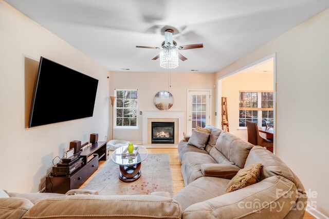 living area with light wood-style floors, a glass covered fireplace, and ceiling fan