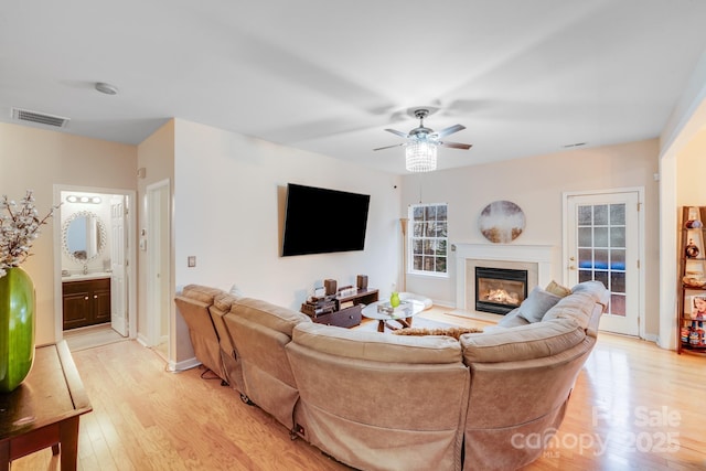 living area with visible vents, baseboards, a glass covered fireplace, light wood-style flooring, and ceiling fan