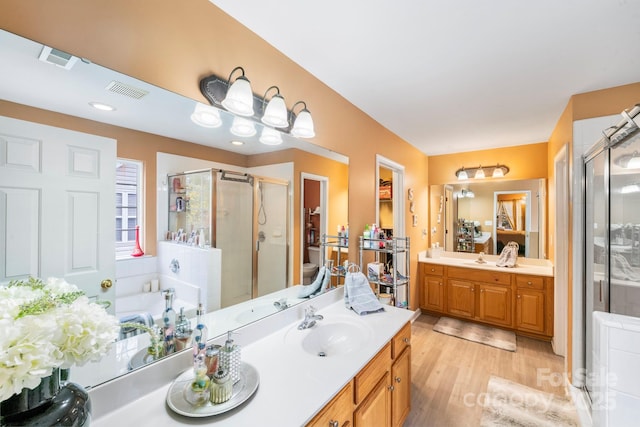 full bath featuring wood finished floors, two vanities, a sink, visible vents, and a shower stall