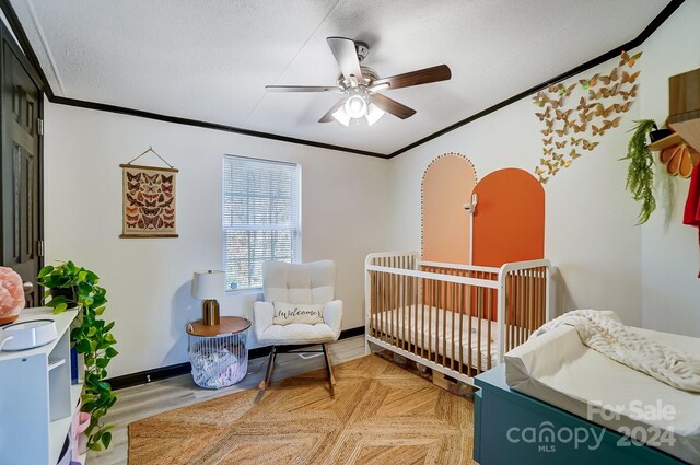 bedroom with ceiling fan, crown molding, a crib, and a textured ceiling