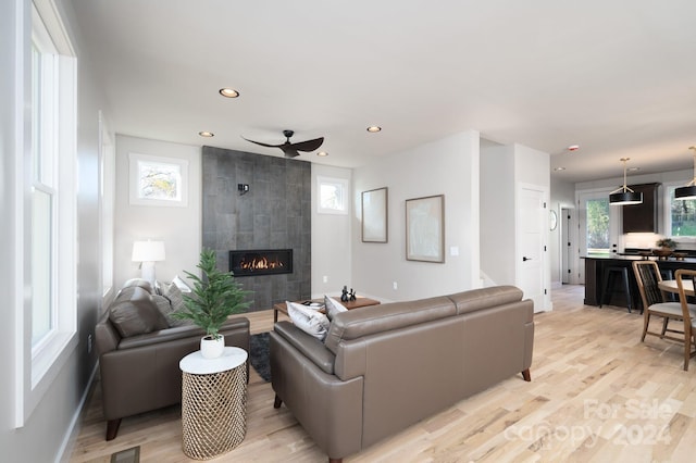 living room with a tile fireplace, light hardwood / wood-style floors, ceiling fan, and a healthy amount of sunlight