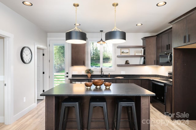 kitchen with a kitchen breakfast bar, dark brown cabinets, black appliances, light hardwood / wood-style floors, and a kitchen island