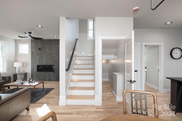 stairway featuring ceiling fan, wood-type flooring, and a tiled fireplace