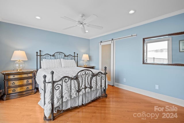 bedroom featuring a barn door, hardwood / wood-style flooring, ceiling fan, and ornamental molding