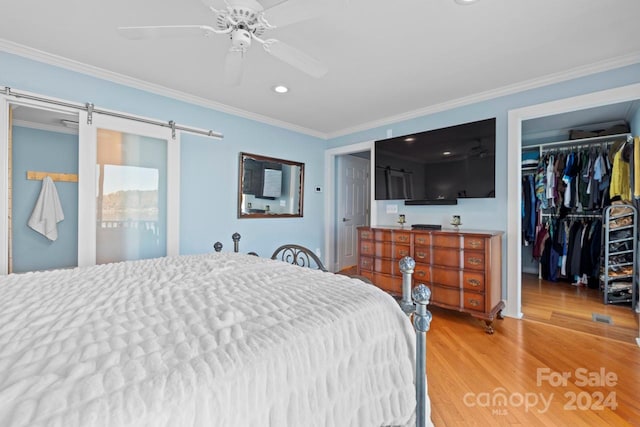 bedroom with a barn door, ceiling fan, hardwood / wood-style floors, and ornamental molding