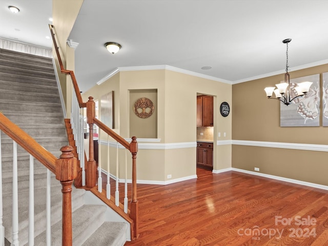 stairway with a chandelier, wood-type flooring, and crown molding