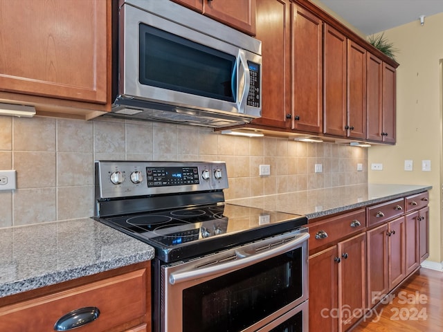 kitchen with stainless steel appliances, light hardwood / wood-style flooring, tasteful backsplash, and light stone counters