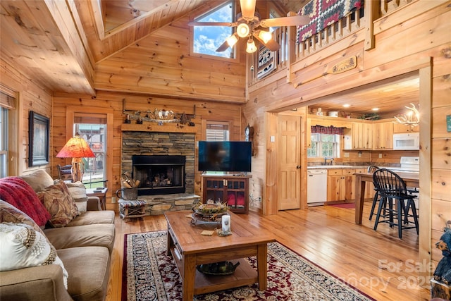 living room featuring ceiling fan, wooden walls, a stone fireplace, and light wood-type flooring