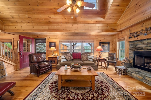 living room featuring a stone fireplace, light hardwood / wood-style flooring, wooden ceiling, and wood walls