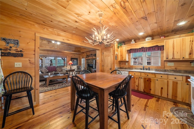 dining room with sink, wood walls, an inviting chandelier, light wood-type flooring, and wooden ceiling