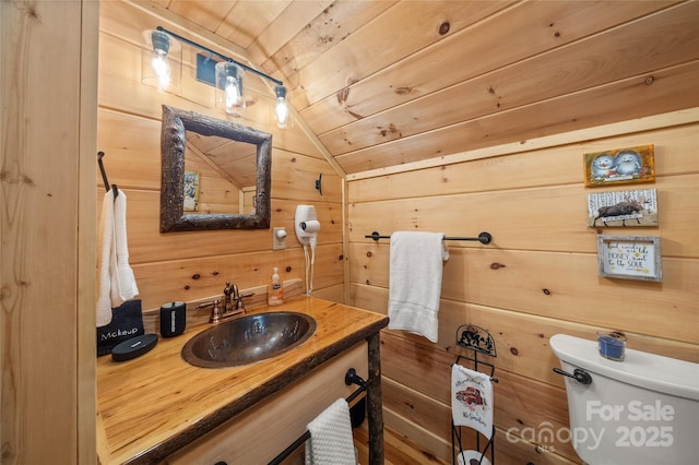 bathroom featuring wood ceiling, vanity, vaulted ceiling, toilet, and wood walls