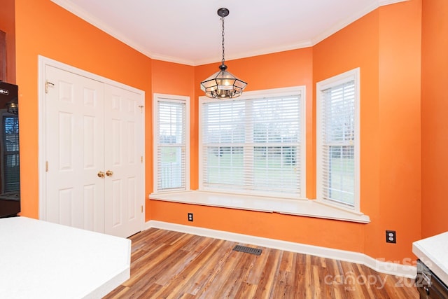 unfurnished dining area with wood-type flooring, ornamental molding, and an inviting chandelier