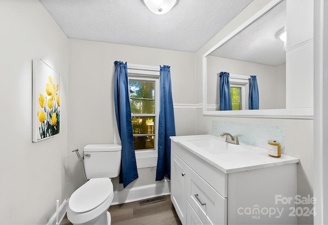 bathroom with a textured ceiling, hardwood / wood-style flooring, toilet, and a wealth of natural light