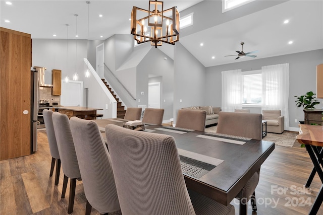 dining space with ceiling fan with notable chandelier, light wood-type flooring, and high vaulted ceiling