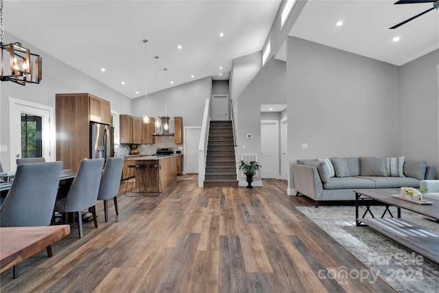 living room featuring dark hardwood / wood-style flooring, high vaulted ceiling, and ceiling fan with notable chandelier