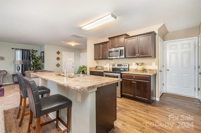 kitchen featuring a breakfast bar, a center island with sink, sink, light hardwood / wood-style floors, and stainless steel appliances