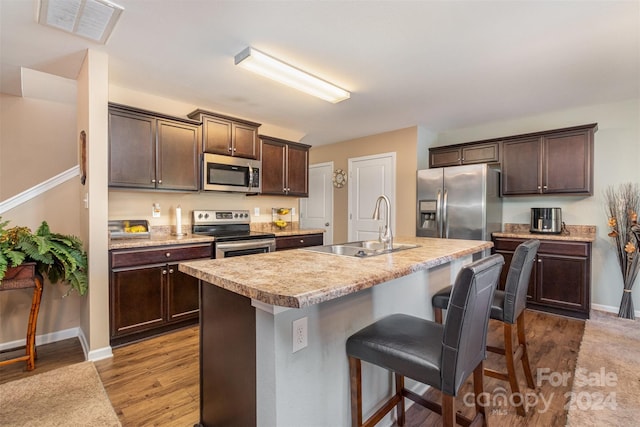 kitchen featuring a breakfast bar, a kitchen island with sink, dark wood-type flooring, sink, and stainless steel appliances