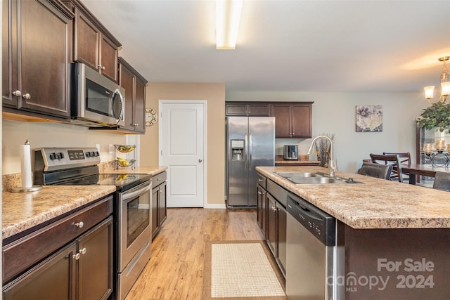 kitchen with appliances with stainless steel finishes, dark brown cabinetry, sink, a center island with sink, and light hardwood / wood-style floors