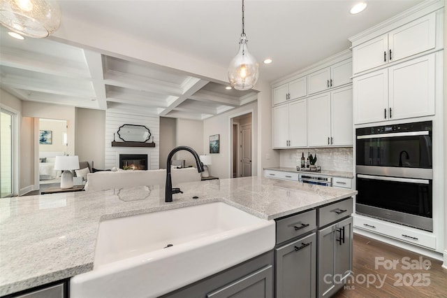 kitchen featuring stainless steel double oven, gray cabinetry, coffered ceiling, a fireplace, and a sink