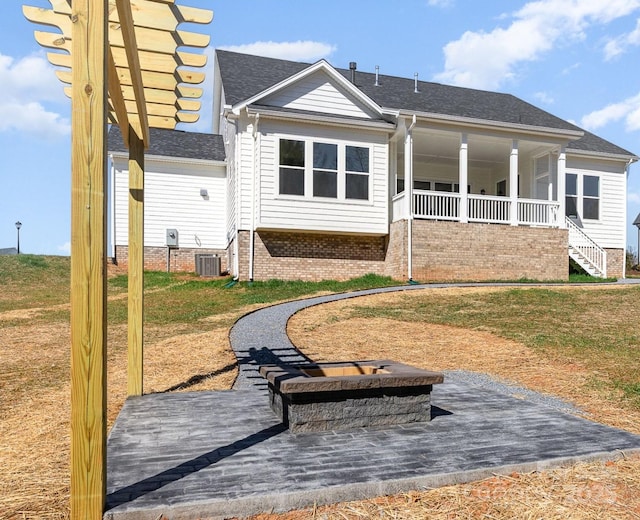 rear view of house featuring central air condition unit, a shingled roof, a porch, and a yard