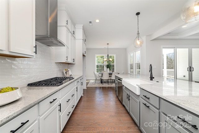 kitchen featuring dark wood-style floors, stainless steel appliances, gray cabinets, a sink, and wall chimney range hood