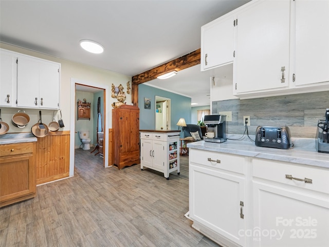 kitchen with white cabinetry, decorative backsplash, beam ceiling, and light wood-type flooring