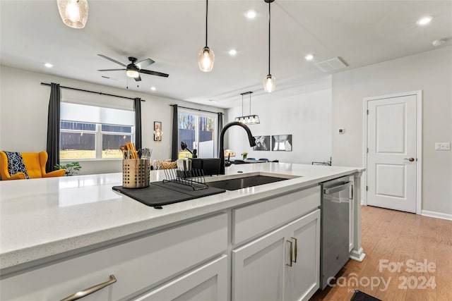 kitchen with light wood-type flooring, stainless steel dishwasher, sink, white cabinetry, and hanging light fixtures