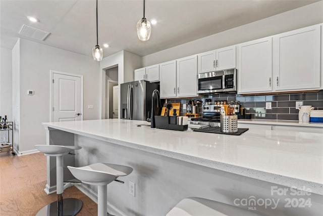 kitchen with tasteful backsplash, stainless steel appliances, decorative light fixtures, light hardwood / wood-style floors, and white cabinetry