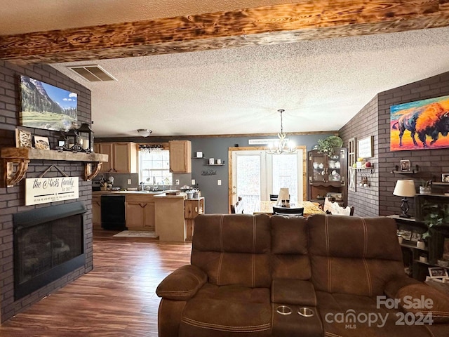 living room with hardwood / wood-style floors, a brick fireplace, beamed ceiling, a notable chandelier, and brick wall