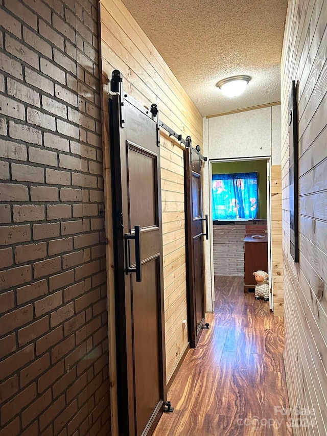 corridor featuring a barn door, dark hardwood / wood-style flooring, brick wall, a textured ceiling, and wooden walls