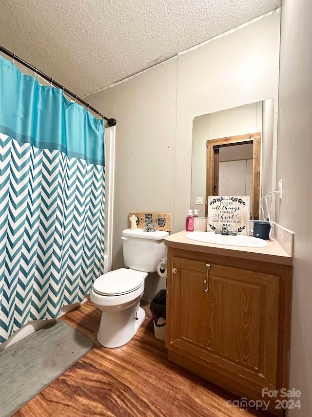 bathroom with hardwood / wood-style floors, vanity, toilet, a textured ceiling, and walk in shower