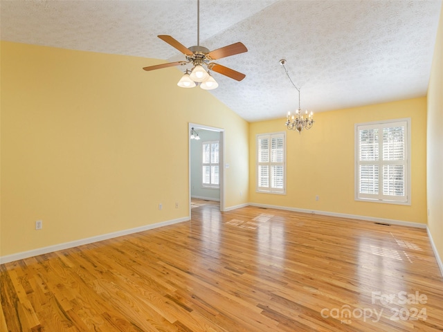 empty room with ceiling fan with notable chandelier, a textured ceiling, light hardwood / wood-style flooring, and vaulted ceiling