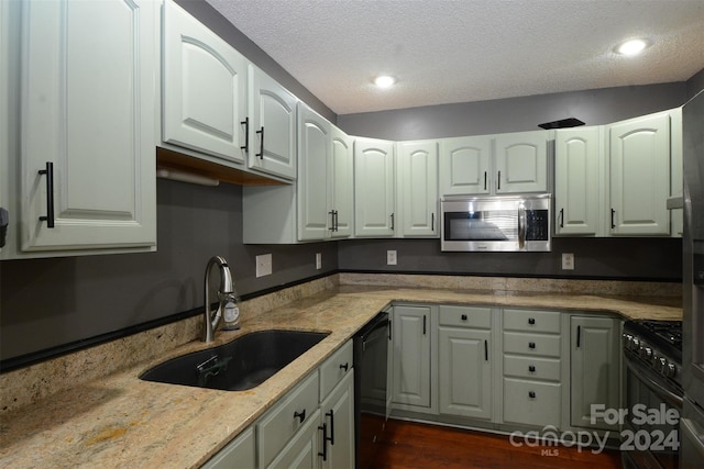 kitchen featuring dishwasher, sink, dark wood-type flooring, gas range oven, and a textured ceiling