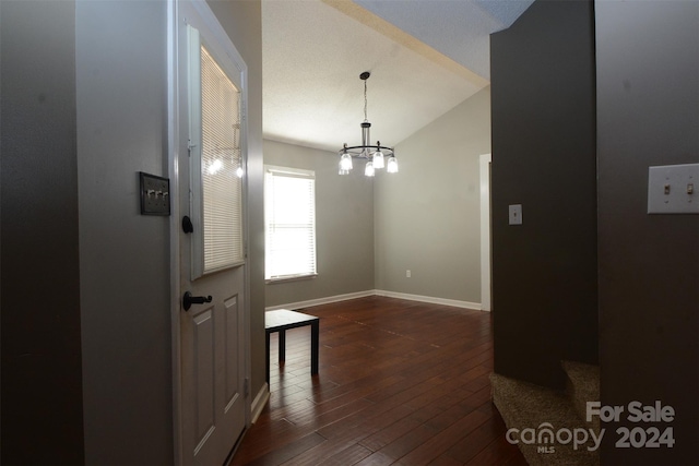 corridor with vaulted ceiling, dark wood-type flooring, and a notable chandelier