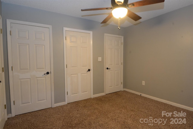 unfurnished bedroom featuring carpet, ceiling fan, and multiple closets