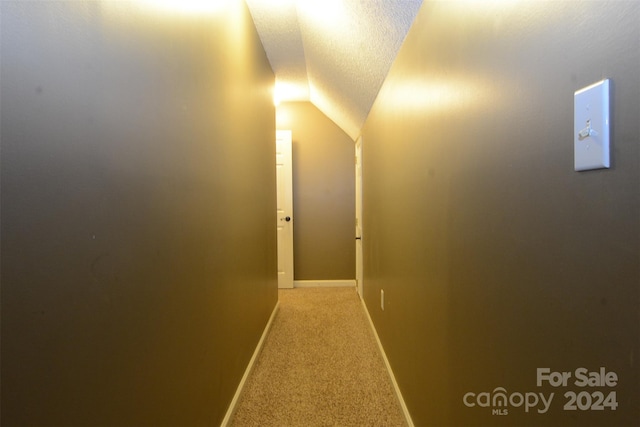 corridor with a textured ceiling, carpet floors, and lofted ceiling