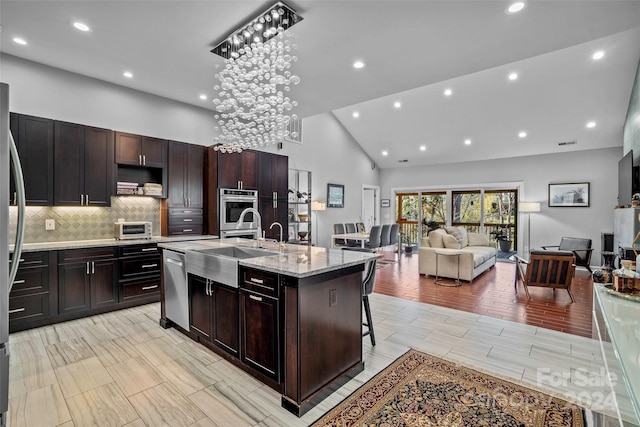 kitchen featuring high vaulted ceiling, light hardwood / wood-style floors, a breakfast bar area, a kitchen island with sink, and appliances with stainless steel finishes