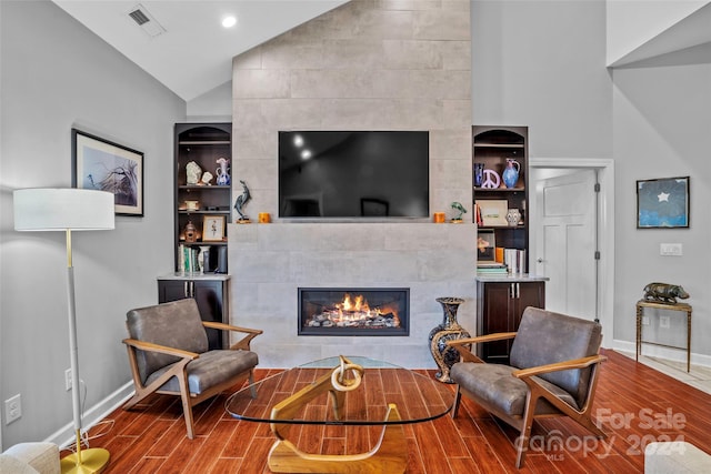 living room featuring built in features, wood-type flooring, a tiled fireplace, and vaulted ceiling