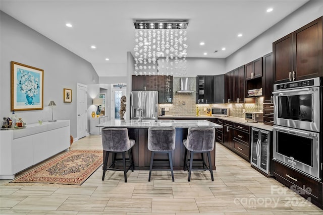 kitchen featuring a breakfast bar, wine cooler, wall chimney exhaust hood, an island with sink, and appliances with stainless steel finishes