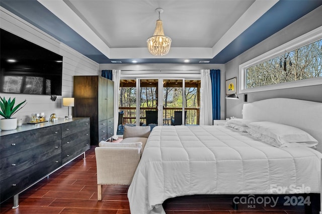 bedroom with a tray ceiling, dark wood-type flooring, access to outside, and a notable chandelier