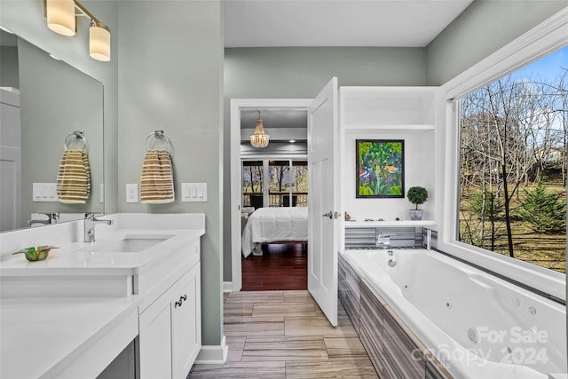 bathroom with hardwood / wood-style floors, plenty of natural light, tiled tub, and vanity