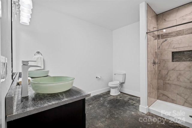 bathroom with a tile shower, vanity, concrete floors, and toilet