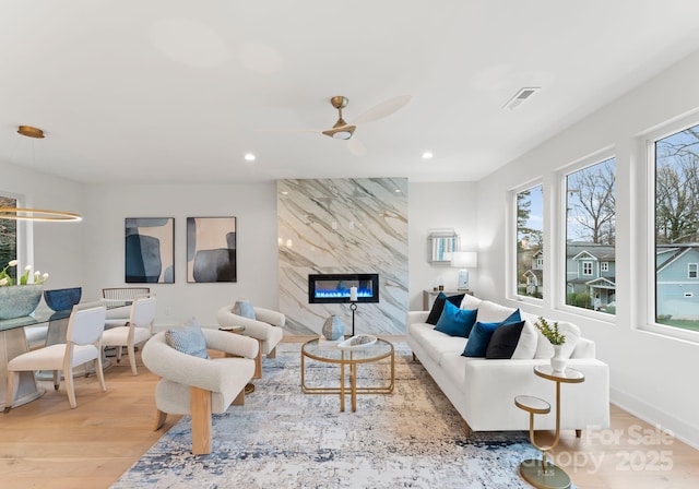 living room featuring ceiling fan, a high end fireplace, and light hardwood / wood-style flooring