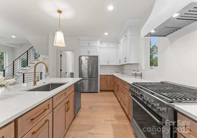 kitchen with pendant lighting, white cabinets, sink, appliances with stainless steel finishes, and custom range hood