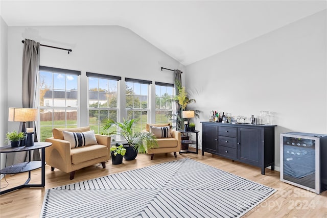 sitting room with wine cooler, light hardwood / wood-style flooring, indoor bar, and vaulted ceiling